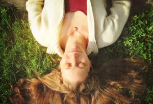 Woman laying on green grass with eyes closed receiving supportive reiki.